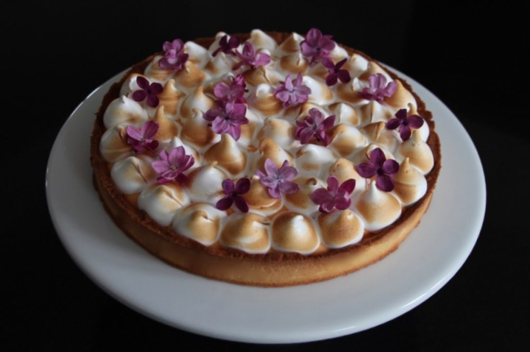 Tarte au citron meringuée traditionnelle décorée de fleurs violettes sur assiette blanche