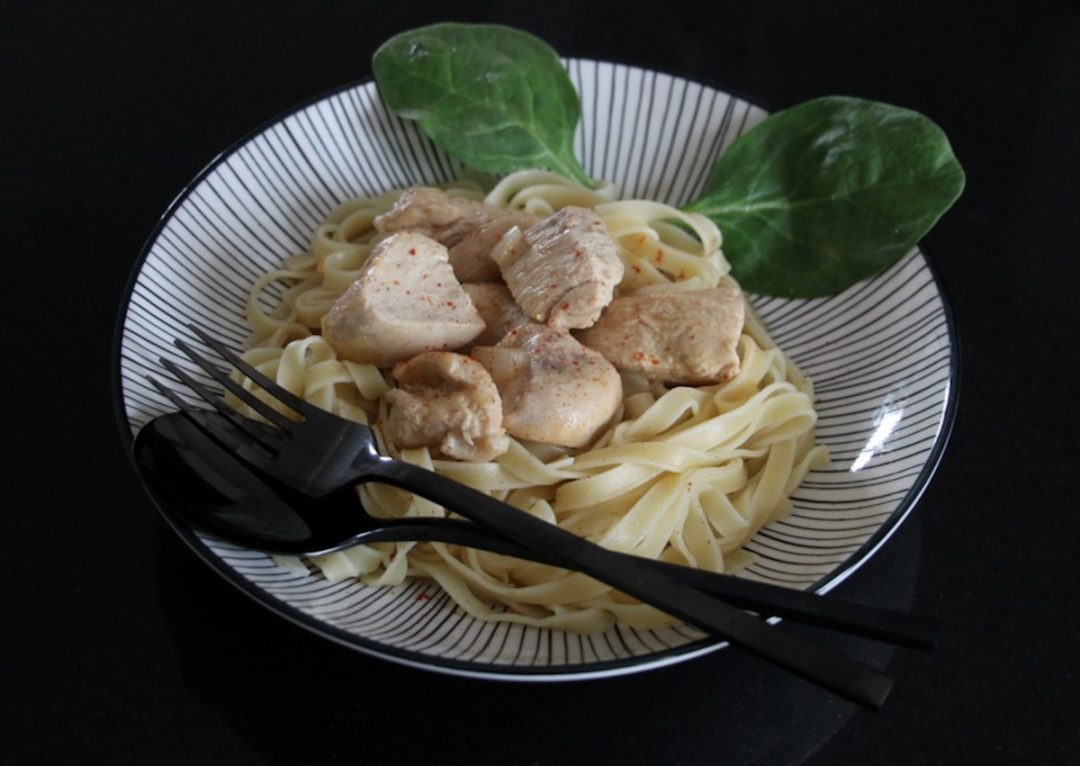 Morceaux de poulet cumin crémeux sur tagliatelles, décoré de feuilles vertes