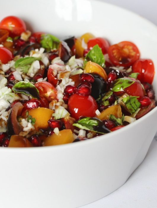 Salade grenade colorée avec tomates cerises, basilic et grains de grenade dans un bol blanc