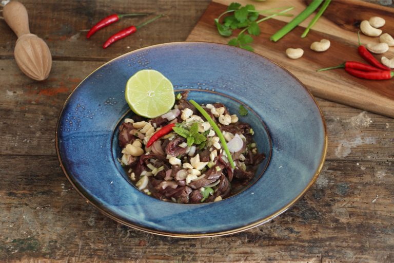 Salade boeuf thai servie dans un bol bleu avec citron vert et piments rouges