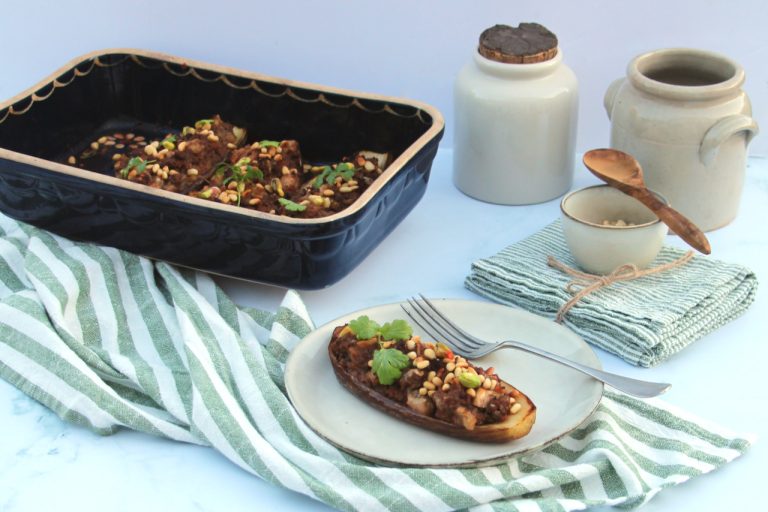 Aubergine farcie à la viande hachée, parsemée de pignons, sur assiette blanche