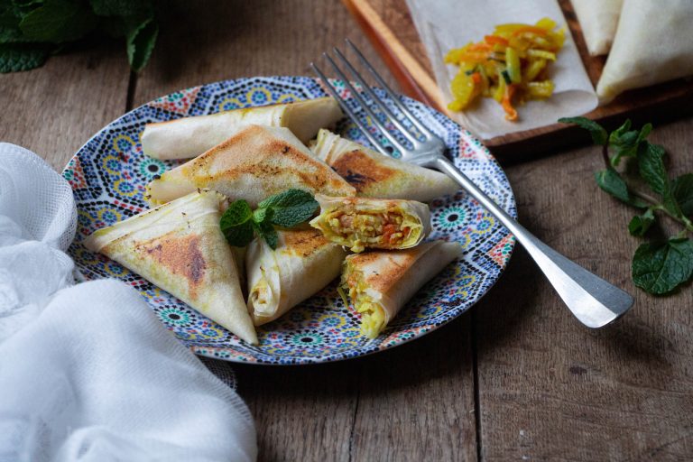 Assiette colorée de samoussas dorés aux légumes et curry, garnis de menthe fraîche