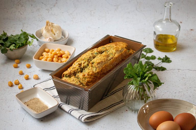 Cake pois chiche doré dans moule entouré d'ingrédients frais et épices