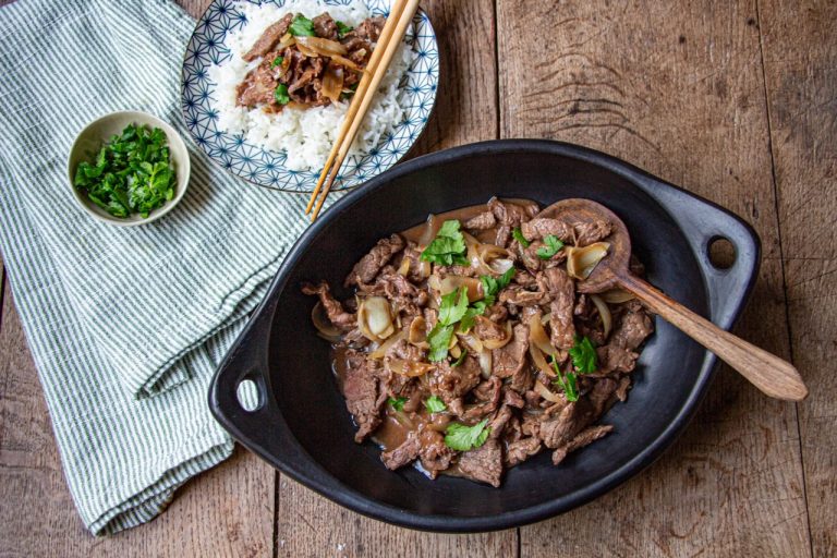 Plat de boeuf aux oignons garni de coriandre, servi dans un plat noir rustique