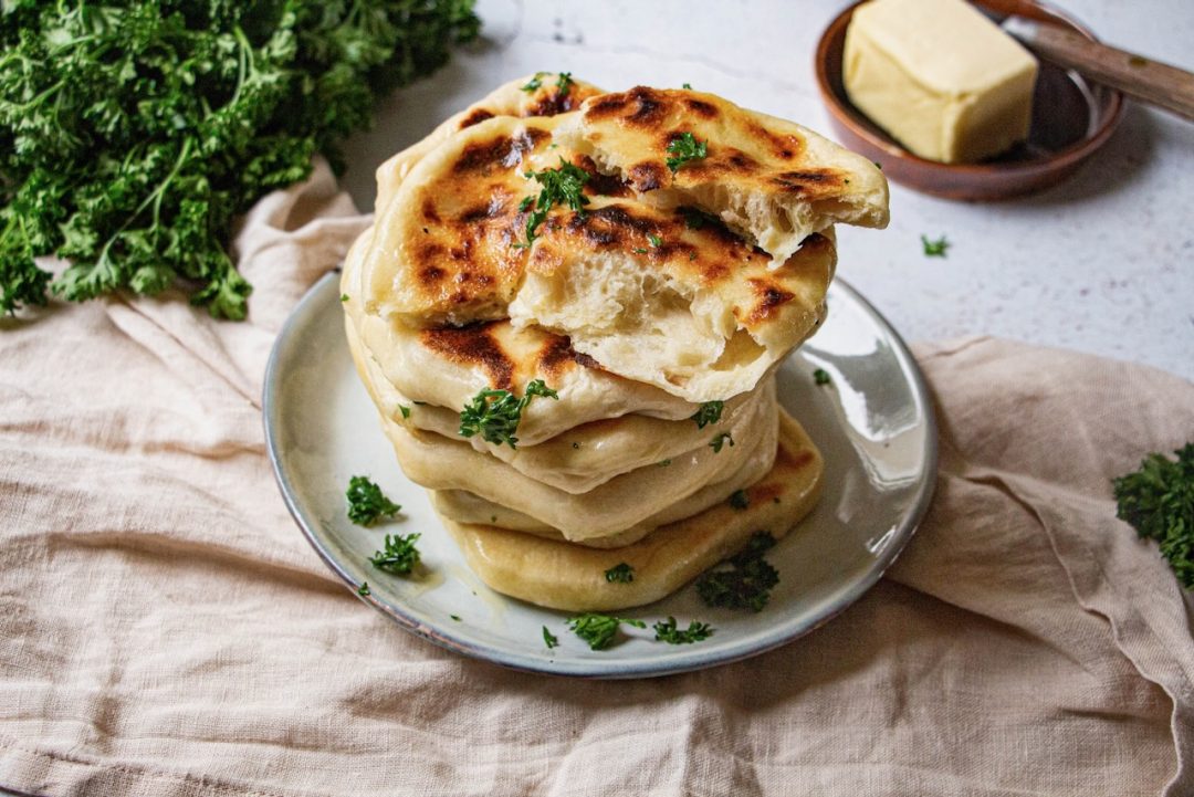 Pile de cheese naan dorés avec persil frais sur assiette blanche