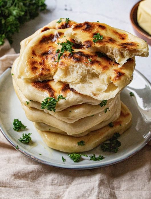 Pile de cheese naan dorés avec persil frais sur assiette blanche