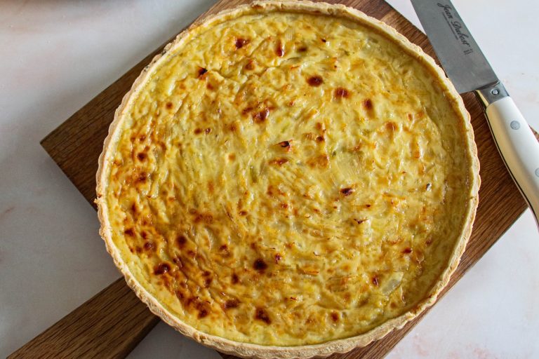 Tarte à l'oignon alsacienne dorée sur planche en bois avec couteau visible