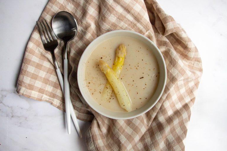 Bol de velouté d'asperges garni de deux asperges blanches sur nappe à carreaux