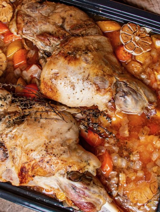 Deux gigots d'agneau dorés avec carottes, oignons et ail, dans un plat en sauce