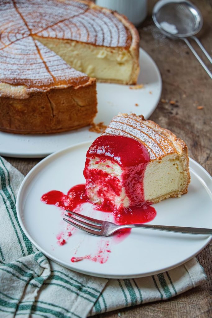 Part de tarte au fromage blanc nappée de coulis rouge sur assiette blanche