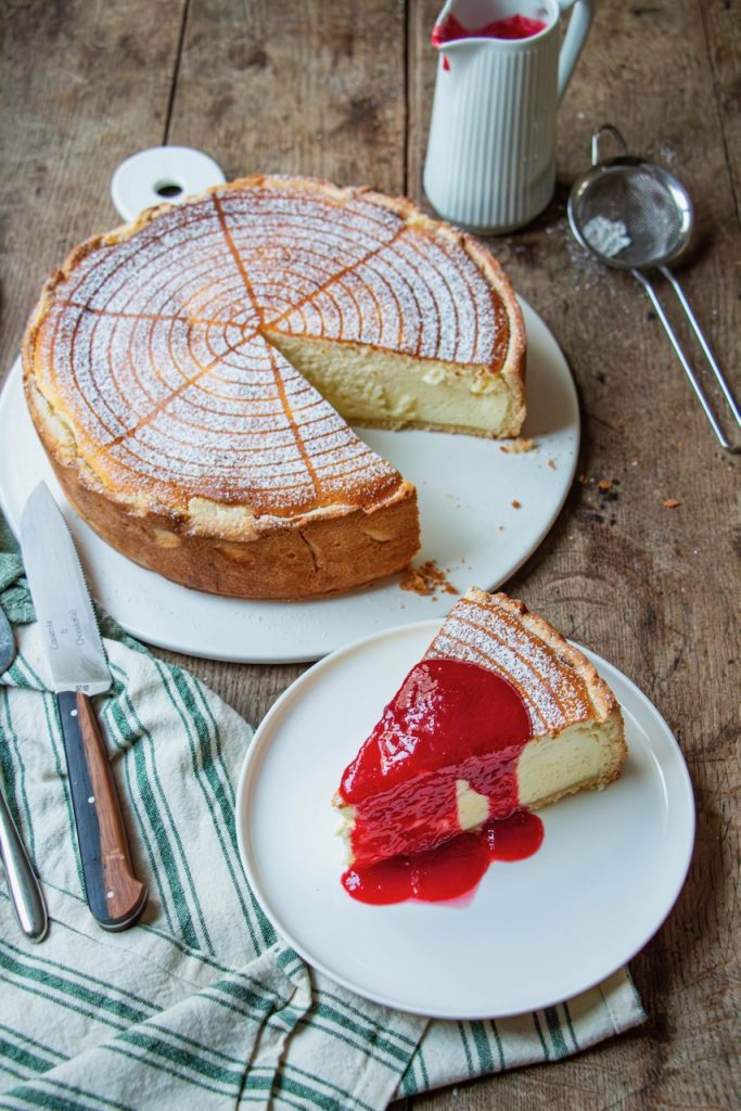 Gros plan d'une part de tarte au fromage blanc nappée de coulis rouge