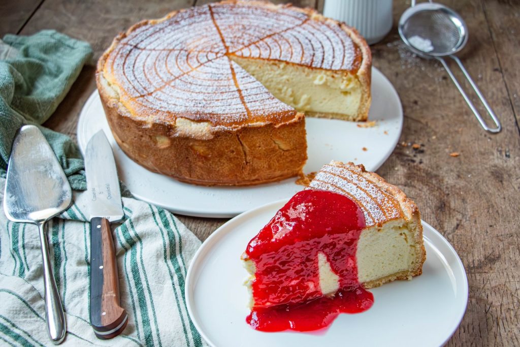 Part de tarte au fromage blanc nappée de coulis rouge sur assiette blanche