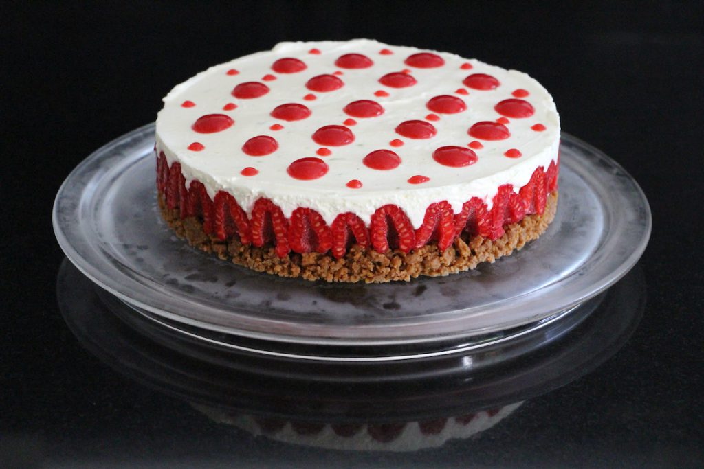 Cheesecake sans cuisson sur assiette transparente, décoré de framboises et coulis rouge