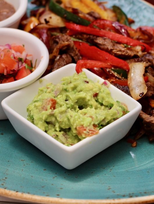 Guacamole crémeux dans un bol blanc, entouré de légumes colorés, recette guacamole traditionnel