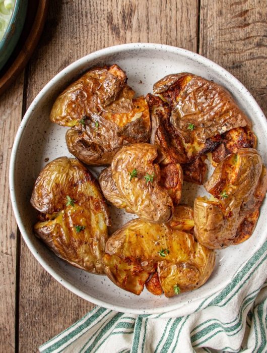 Smashed potatoes dorés avec herbes dans un plat blanc sur table en bois