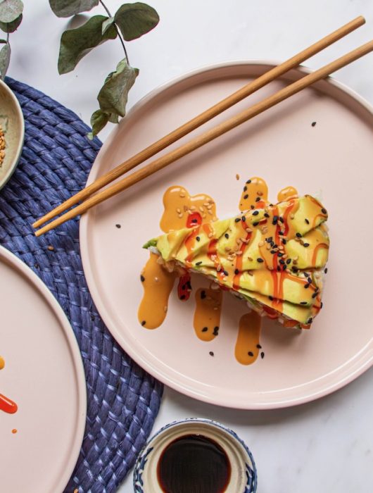Tranche de Sushi Cake Avocat Saumon garnie de sauces colorées et graines de sésame