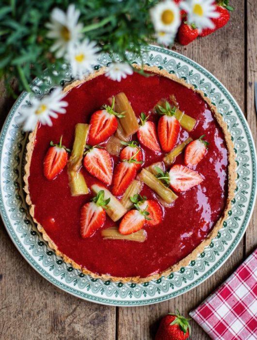 Tarte rhubarbe fraise avec fraises fraîches et morceaux de rhubarbe sur assiette décorée
